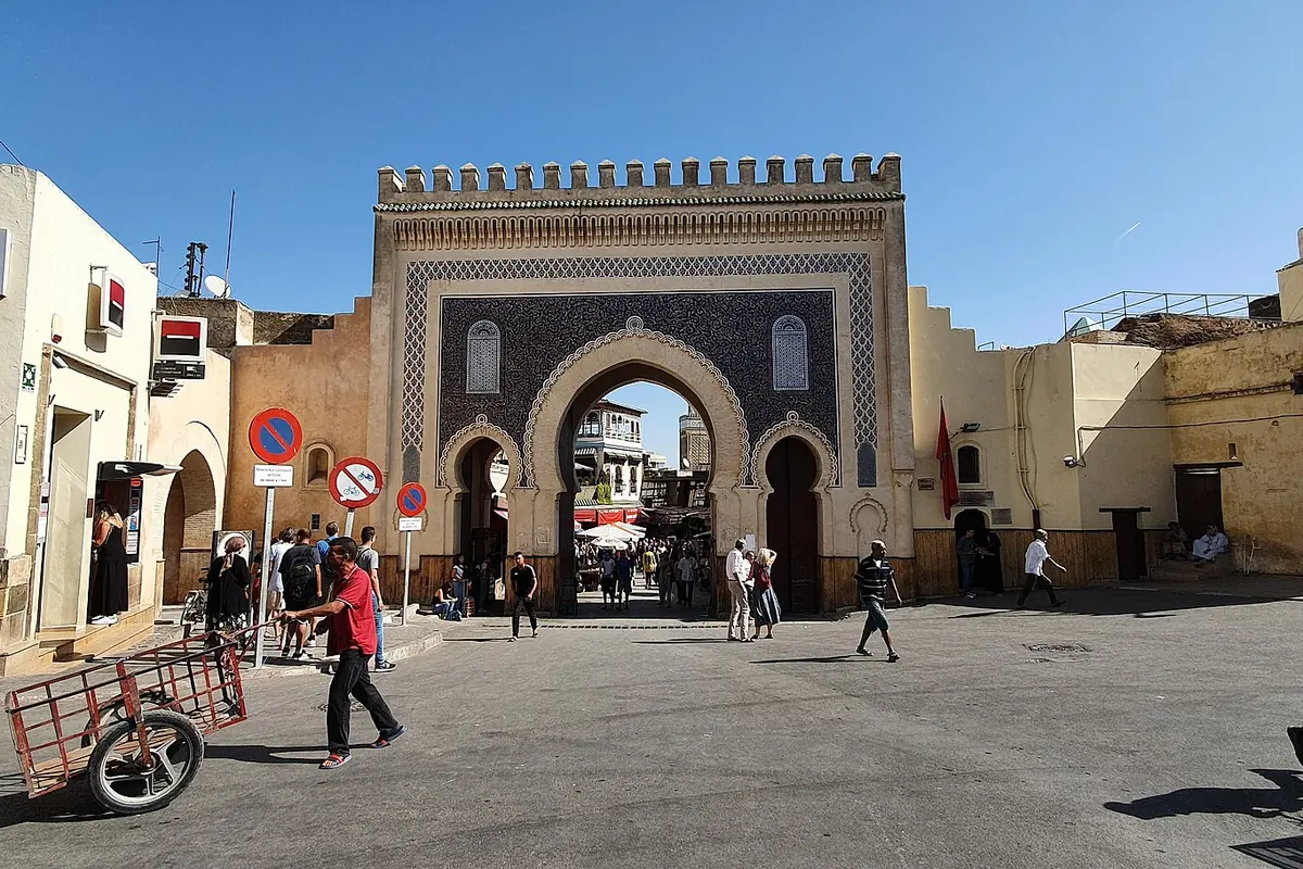The blue-tiled Bab Bou Jeloud gate in the wall of the old city of Fes, with people crossing the open square in front of it