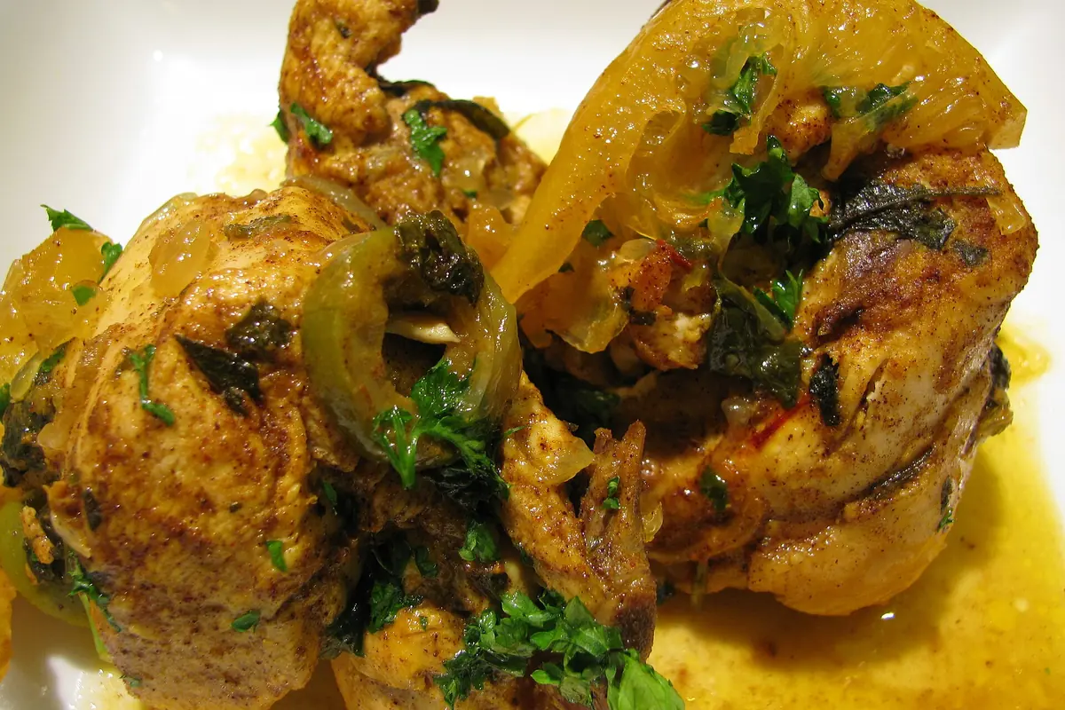 Chicken pieces in a golden sauce with preserved lemon and fresh herbs, a Moroccan tagine served on a white plate