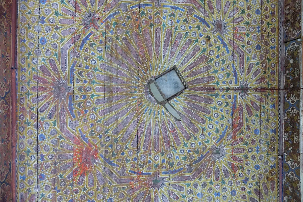 A painted and carved wooden ceiling with a star-shaped pattern radiating from a central lantern opening.